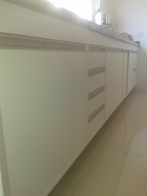 Gabinete de cozinha em MDF branco na parte interna e externa, com puxador de alumínio embutido, tipo cava.