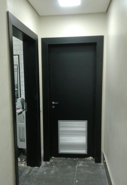 Porta Entrada Sanitário, com batente e guarnição revestida em fórmica preta texturizada, com grelha de ventilação de alumínio.